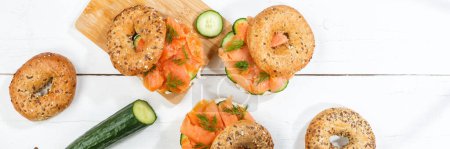 Photo for Bagel sandwich with salmon fish and cream cheese for breakfast panorama on a wooden board from above - Royalty Free Image