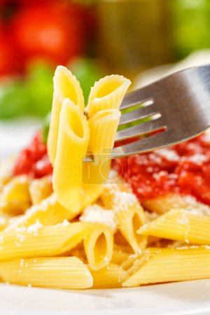 Téléchargez les photos : Penne Rigatoni Rigate manger des pâtes italiennes manger à la fourchette déjeuner avec sauce tomate sur une assiette format portrait - en image libre de droit