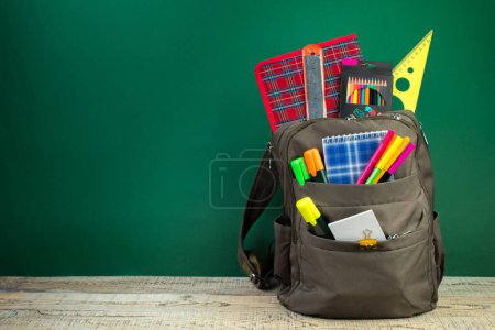 Photo for Backpack with different colorful stationery on table. Green background. Back to school - Royalty Free Image
