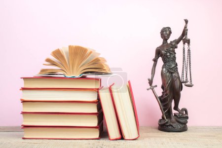 Photo for Law concept - Open law book, Judge's gavel, scales, Themis statue on table in a courtroom or law enforcement office. Wooden table, pink background. - Royalty Free Image