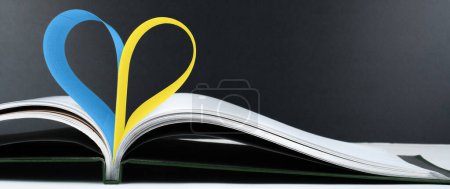 Photo for Open book with blue and yellow heart shaped pages on a black background.. The concept of education in Ukraine. - Royalty Free Image