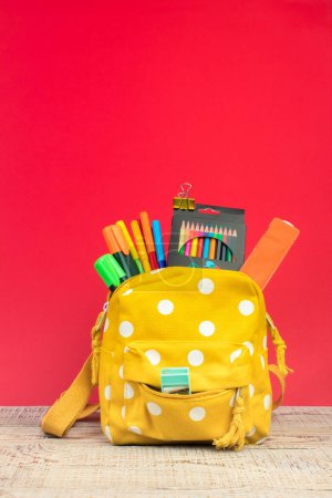 Photo for Backpack with different colorful stationery on table. Bright Red background. Back to school - Royalty Free Image