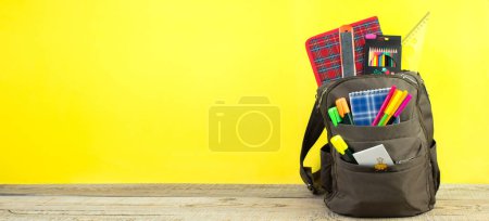 Photo for Backpack with different colorful stationery on table. Yellow background. Back to school - Royalty Free Image