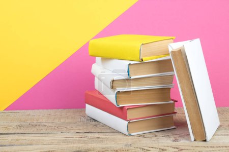 Photo for Books stacking. Books on wooden table and pink, yellow background. Back to school. Copy space for ad text - Royalty Free Image
