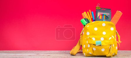 Foto de Mochila con diferentes artículos de papelería de colores en la mesa. Fondo rojo brillante. Regreso a la escuela - Imagen libre de derechos