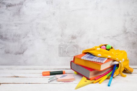 Photo for Yellow backpack with white polka dots with different colorful stationery on table. gray concrete background. Back to school. Banner design - Royalty Free Image