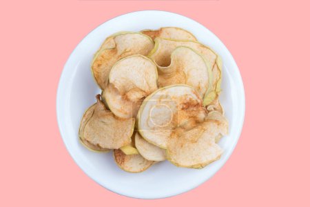 Téléchargez les photos : Pommes tranchées et séchées dans une assiette isolée sur fond rose. Pomme biologique maison - en image libre de droit