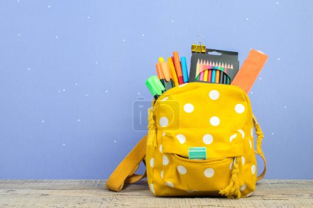 Photo for Backpack with different colorful stationery on table. Purple background. Back to school - Royalty Free Image