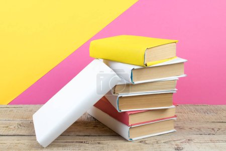 Foto de Libros apilados. Libros sobre mesa de madera y fondo rosa, amarillo. De vuelta a la escuela. Copiar espacio para texto del anuncio - Imagen libre de derechos