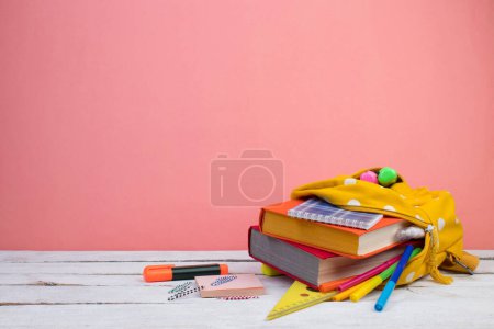 Photo for Backpack with different colorful stationery on table. Pink background. Back to school - Royalty Free Image