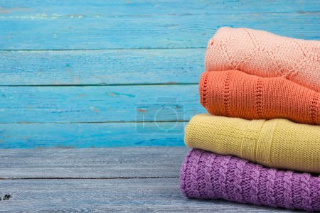 Photo for Knitted wool sweaters. Pile of knitted summer, autumn clothes on blue, wooden background, sweaters, knitwear, space for text. - Royalty Free Image