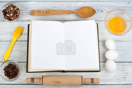 Foto de Receta cocinar libro en blanco sobre fondo de madera, cuchara, rodillo, mantel a cuadros
. - Imagen libre de derechos