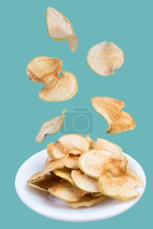 Téléchargez les photos : Des fruits volants. Trancher les pommes séchées dans une assiette isolée sur fond vert. Pomme biologique maison - en image libre de droit