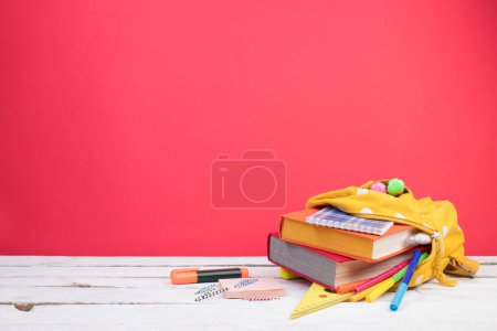 Photo for Backpack with different colorful stationery on table. Bright Red background. Back to school - Royalty Free Image