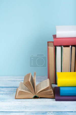 Foto de Apilamiento de libros. Libro abierto, libros de tapa dura sobre mesa de madera y fondo azul. De vuelta a la escuela. Copiar espacio para texto - Imagen libre de derechos
