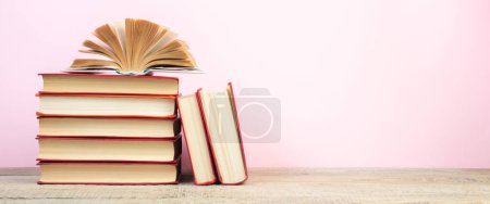 Photo for Composition with hardback books, fanned pages on wooden deck table and pink background. Books stacking. Back to school. Copy Space. Education background. Tuition payment. Banner - Royalty Free Image