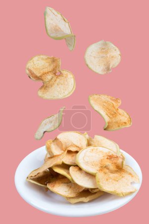 Téléchargez les photos : Des fruits volants. Pommes tranchées et séchées dans une assiette isolée sur fond rose. Pomme biologique maison - en image libre de droit
