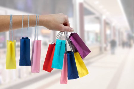 Téléchargez les photos : Crop main féminine tenant des sacs en papier coloré sur le fond du centre commercial - en image libre de droit