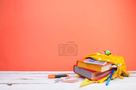 Téléchargez les photos : Sac à dos avec différentes papeterie colorée sur la table. Fond orange. Retour à l'école - en image libre de droit