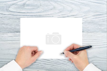 Photo for A hand is writing on a paper on a wooden table. Make notes, make plans, write, draw. Top view with copy space - Royalty Free Image