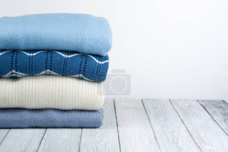 Photo for Knitted wool sweaters. Pile of knitted winter, autumn clothes on white, wooden background, sweaters, knitwear, space for text - Royalty Free Image