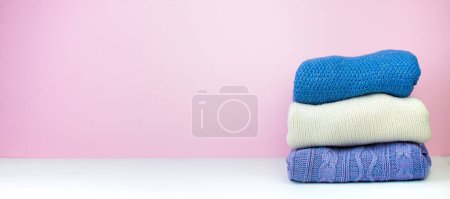 Photo for Knitted woolen sweaters. A bunch of knitted winter, autumn clothing on a pink background, sweaters, knitwear, space for the text. Banner - Royalty Free Image