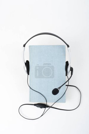 Photo for Audiobook on white background. Headphones put over blue hardback book, empty cover, copy space for ad text. Distance education, e-learning concept - Royalty Free Image