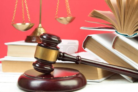 Photo for Law concept - Open law book, Judge's gavel, scales, Themis statue on table in a courtroom or law enforcement office. Wooden table, red background - Royalty Free Image