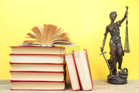 Photo for Law concept - Open law book, Judge's gavel, scales, Themis statue on table in a courtroom or law enforcement office. Wooden table, yellow background. - Royalty Free Image