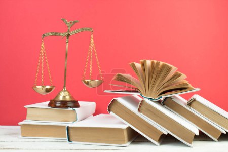 Photo for Law concept - Open law book, Judge's gavel, scales, Themis statue on table in a courtroom or law enforcement office. Wooden table, red background - Royalty Free Image