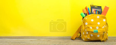 Foto de Mochila con diferentes artículos de papelería de colores en la mesa. Fondo amarillo. Regreso a la escuela. - Imagen libre de derechos