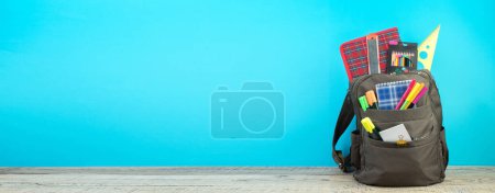 Photo for Backpack with different colorful stationery on table. Blue background. Back to school - Royalty Free Image