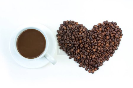Photo for A pile of coffee beans in the shape of a heart, a cup of coffee on a white background. Top view - Royalty Free Image