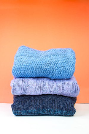 Photo for Knitted woolen sweaters. A bunch of knitted winter, autumn clothing on an orange background, sweaters, knitwear, space for the text. Banner - Royalty Free Image