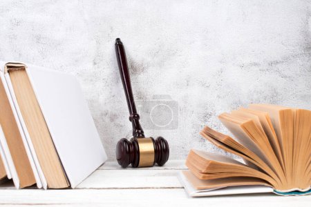 Law concept - Open law book, Judge's gavel, scales, Themis statue on table in a courtroom or law enforcement office. Wooden table, gray concrete background