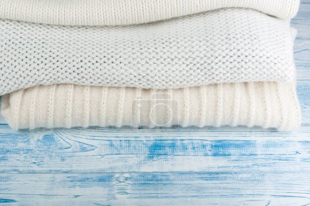 Téléchargez les photos : Pull en laine tricotée. Pile de vêtements d'hiver tricotés sur fond bleu bois, pulls, tricots, espace pour le texte - en image libre de droit