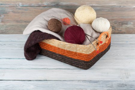 Foto de Bola de lana, agujas y suéter de lana con radios para tejer a mano en canasta sobre mesa de madera - Imagen libre de derechos