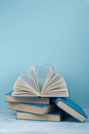 Téléchargez les photos : Empilement de livres. Livre ouvert, livres à dos dur sur table en bois et fond bleu. Je retourne à l'école. Espace de copie pour le texte - en image libre de droit