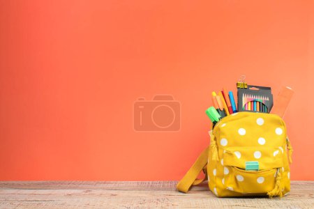 Foto de Mochila con diferentes artículos de papelería de colores en la mesa. Fondo naranja. Regreso a la escuela - Imagen libre de derechos