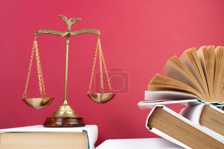 Rechtskonzept - Offenes Gesetzbuch, Richtergabel, Waage, Themis Statue auf dem Tisch im Gerichtssaal oder in der Strafverfolgungsbehörde. Holztisch, roter Hintergrund.