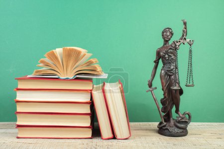 Photo for Law concept - Open law book, Judge's gavel, scales, Themis statue on table in a courtroom or law enforcement office. Wooden table, green background. - Royalty Free Image