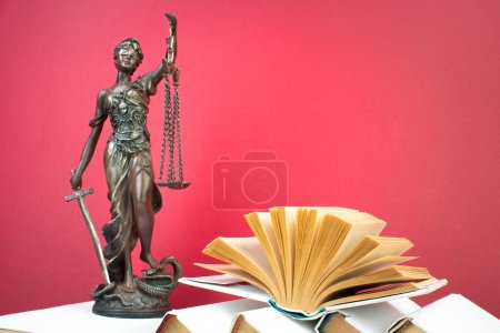 Rechtskonzept - Offenes Gesetzbuch, Richtergabel, Waage, Themis Statue auf dem Tisch im Gerichtssaal oder in der Strafverfolgungsbehörde. Holztisch, roter Hintergrund.