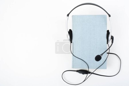 Livre audio sur fond blanc. Écouteurs mis sur le livre bleu hardback, couverture vide, espace de copie pour le texte de l'annonce. Enseignement à distance, concept d'e-learning