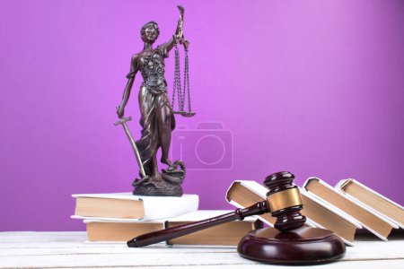 Rechtskonzept - Offenes Gesetzbuch, Richtergabel, Waage, Themis Statue auf dem Tisch im Gerichtssaal oder in der Strafverfolgungsbehörde. Holztisch, lila Hintergrund