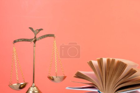 Rechtskonzept - Offenes Gesetzbuch, Richtergabel, Waage, Themis Statue auf dem Tisch im Gerichtssaal oder in der Strafverfolgungsbehörde. Holztisch, oranger Hintergrund