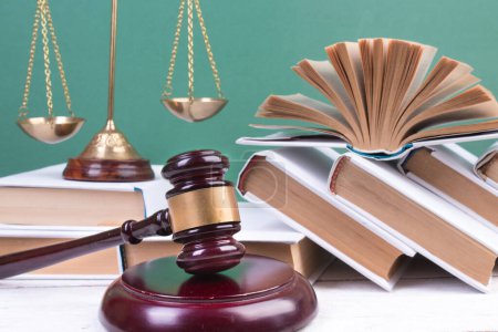Photo for Law concept - Open law book, Judge's gavel, scales, Themis statue on table in a courtroom or law enforcement office. Wooden table, green background. - Royalty Free Image