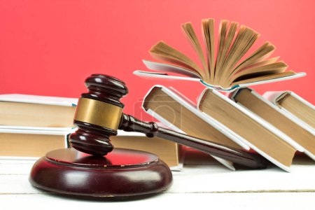 Rechtskonzept - Offenes Gesetzbuch, Richtergabel, Waage, Themis Statue auf dem Tisch im Gerichtssaal oder in der Strafverfolgungsbehörde. Holztisch, roter Hintergrund