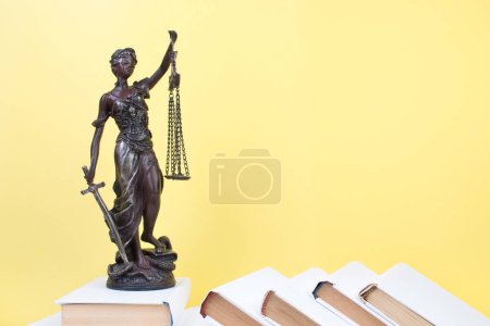 Rechtskonzept - Offenes Gesetzbuch, Richtergabel, Waage, Themis Statue auf dem Tisch im Gerichtssaal oder in der Strafverfolgungsbehörde. Holztisch, gelber Hintergrund