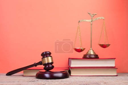 Photo for Law concept - Open law book, Judge's gavel, scales, Themis statue on table in a courtroom or law enforcement office. Wooden table, red background. - Royalty Free Image