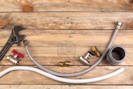 Fittings, pipe, valves, plastic pipe for water, adjustable wrench on the wooden background. Top view. Copy space for text